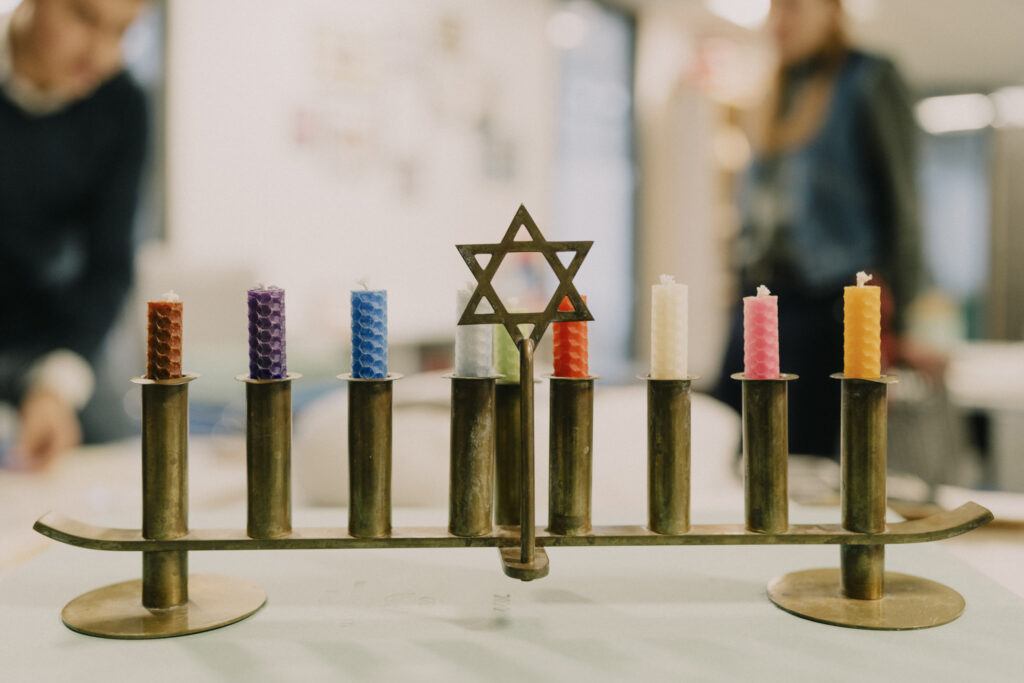 A metal menorah with a King David star in the centre and holding brightly coloured candles